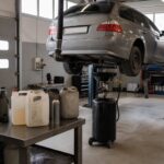 Bil på løftelift i et autoværksted med udsugningsslange på udstødningen, olieopsamler og dunke på et arbejdsbord